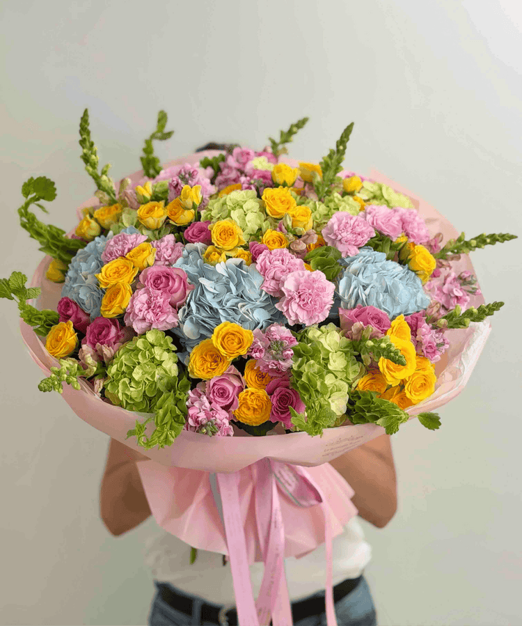 Colorful dopamine bouquet featuring blue hydrangeas, yellow spray roses, pink roses, carnations, and seasonal garden flowers.