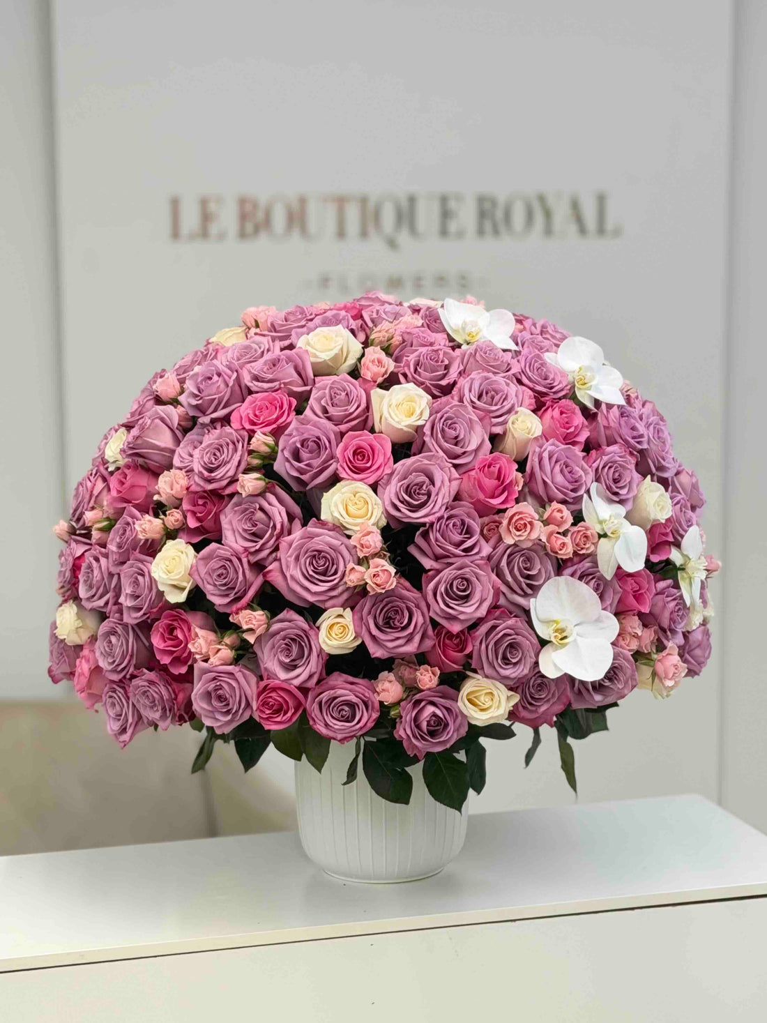 Luxury arrangement of lavender roses, pink spray roses, ivory roses, and white orchids in an elegant vase by Le Boutique Roya