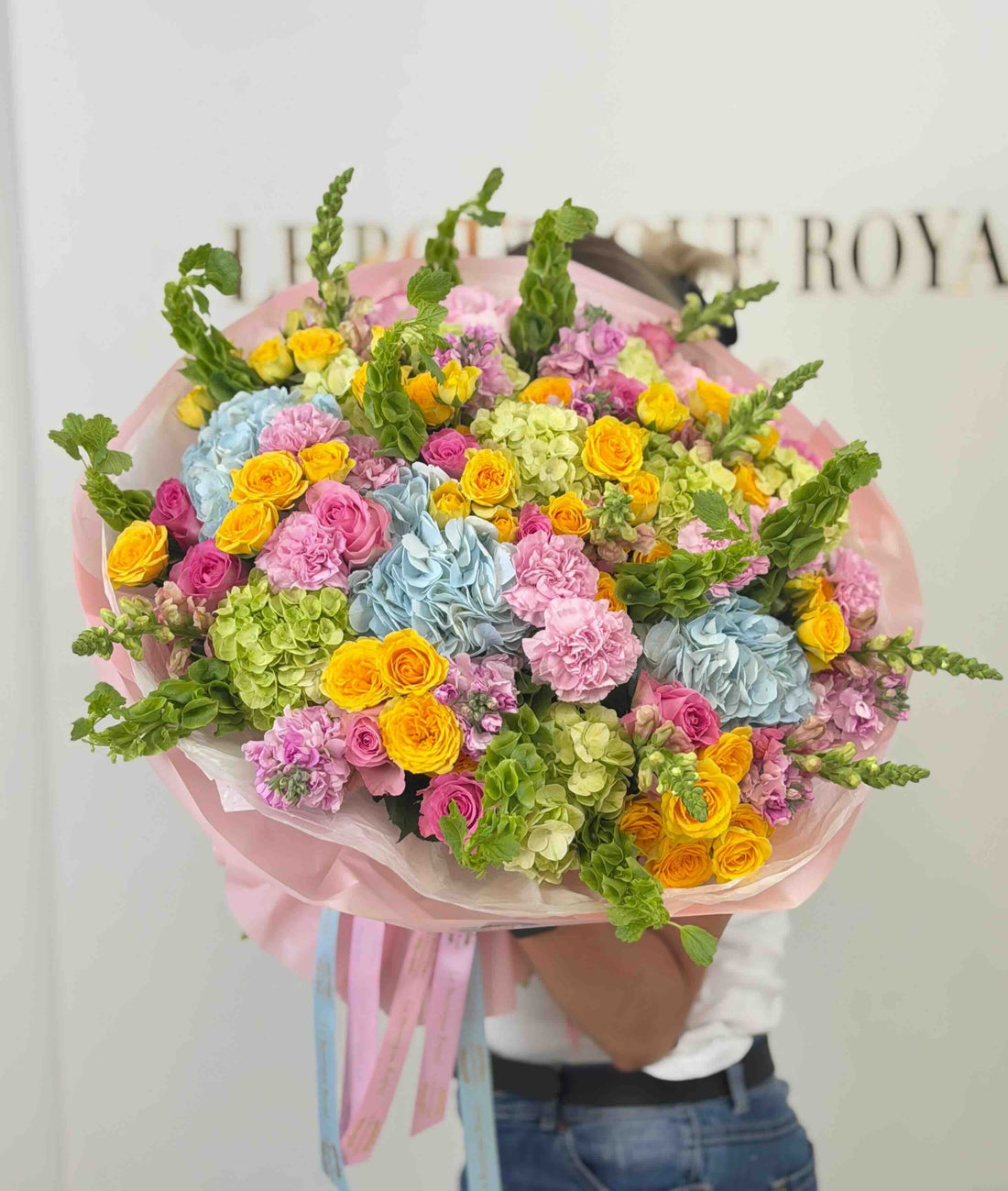 Colorful dopamine bouquet featuring blue hydrangeas, yellow spray roses, pink roses, carnations, and seasonal garden flowers.