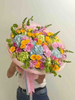 
                    
                      Colorful dopamine bouquet featuring blue hydrangeas, yellow spray roses, pink roses, carnations, and seasonal garden flowers.
                    
                  